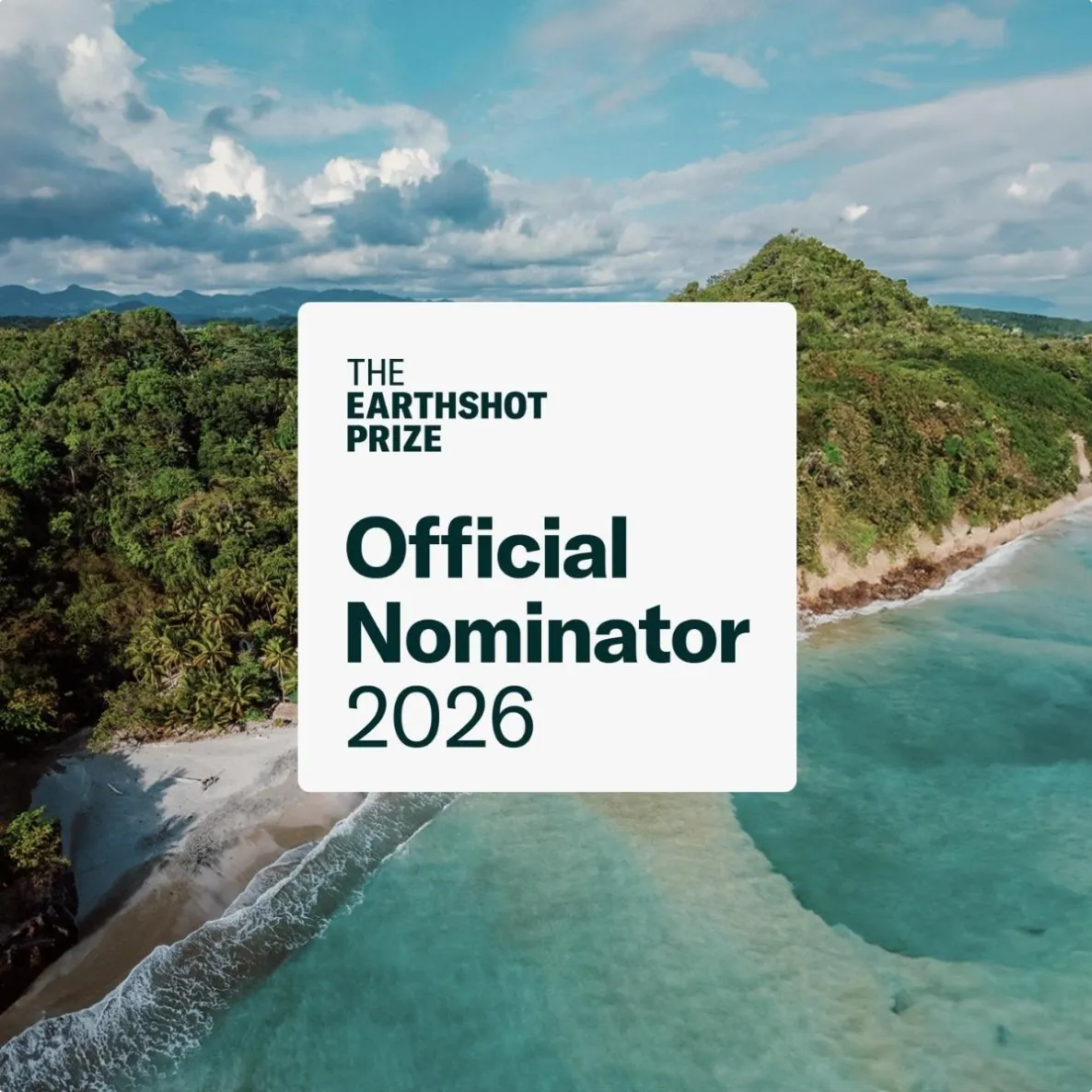 Aerial view of a coastline with green forested hills and blue ocean water, overlaid with a white box stating The Earthshot Prize Official Nominator 2026.