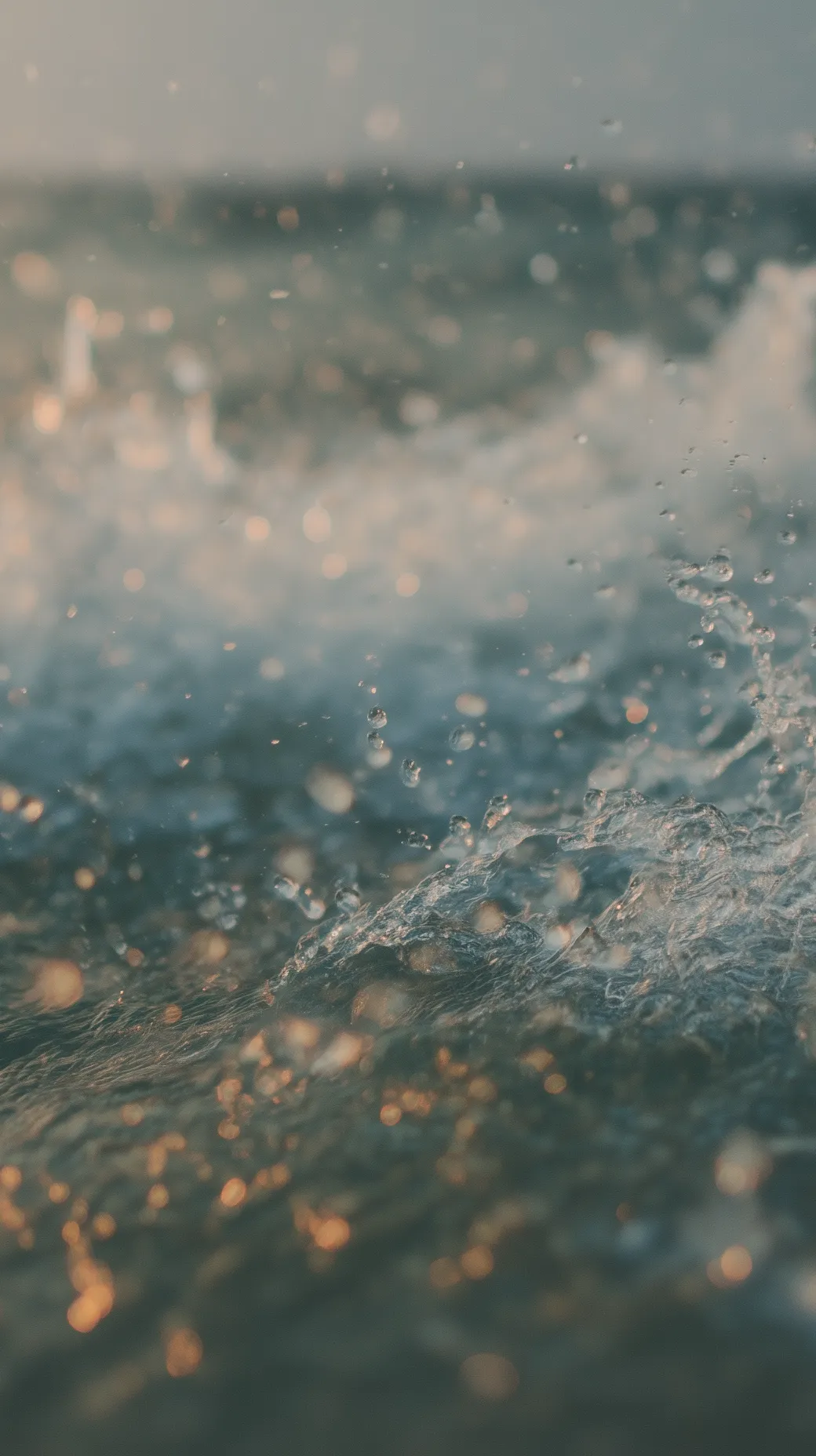 Close-up of ocean water droplets splashing with soft sunlight reflections.