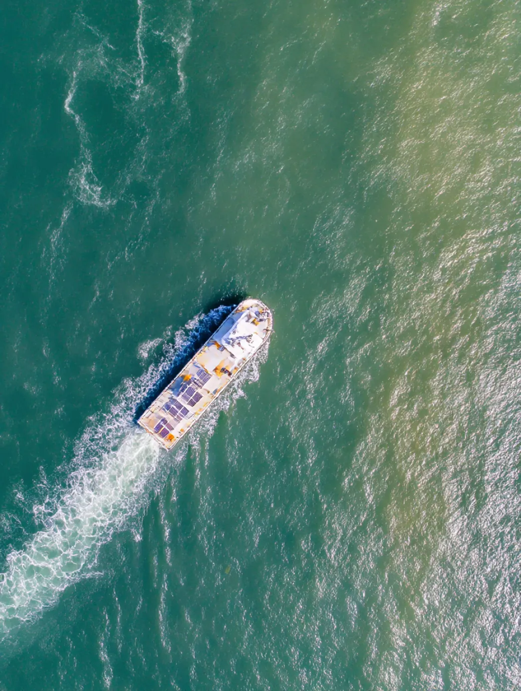 A boat with solar panels on the roof moving across green ocean water, creating a white wake behind.