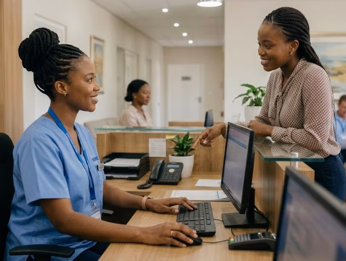 Receptionist in scrubs assisting a smiling woman at a clinic reception desk.