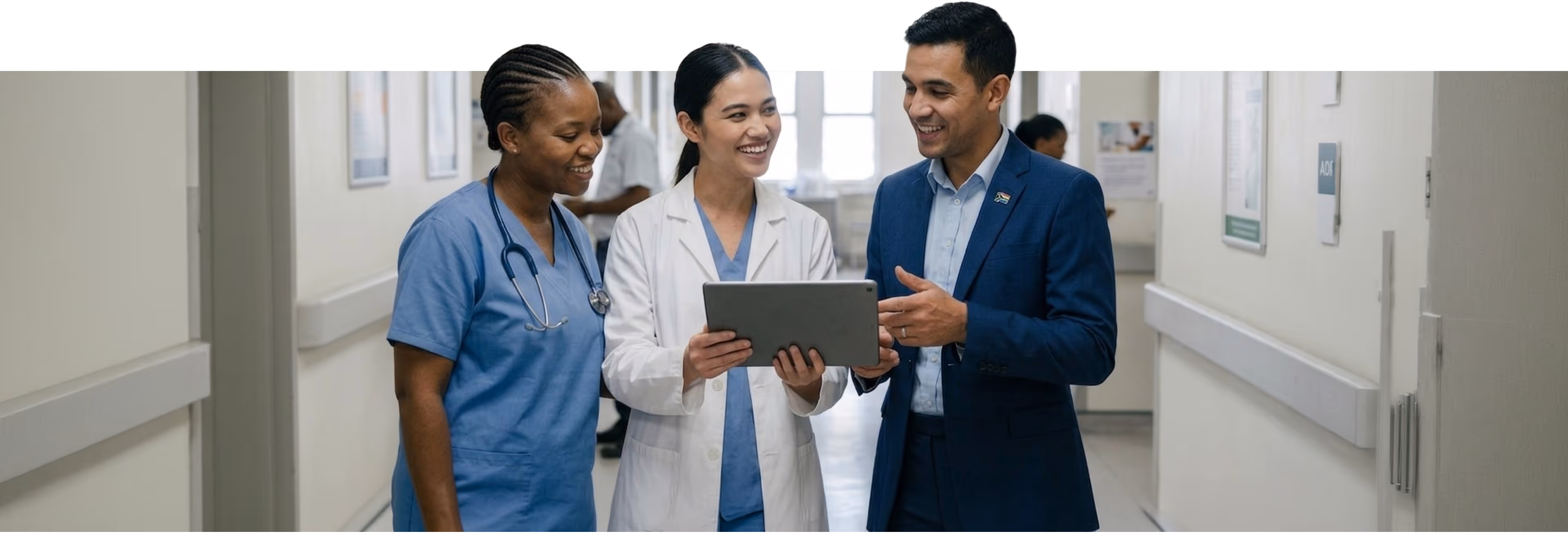 Three healthcare professionals, two women and one man, smiling and discussing while looking at a tablet.