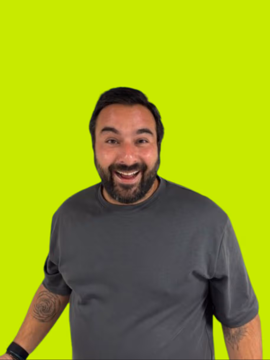 Vrolijke man met een baard en tatoeages op zijn armen, gekleed in een grijs T-shirt, tegen een felgroene achtergrond.