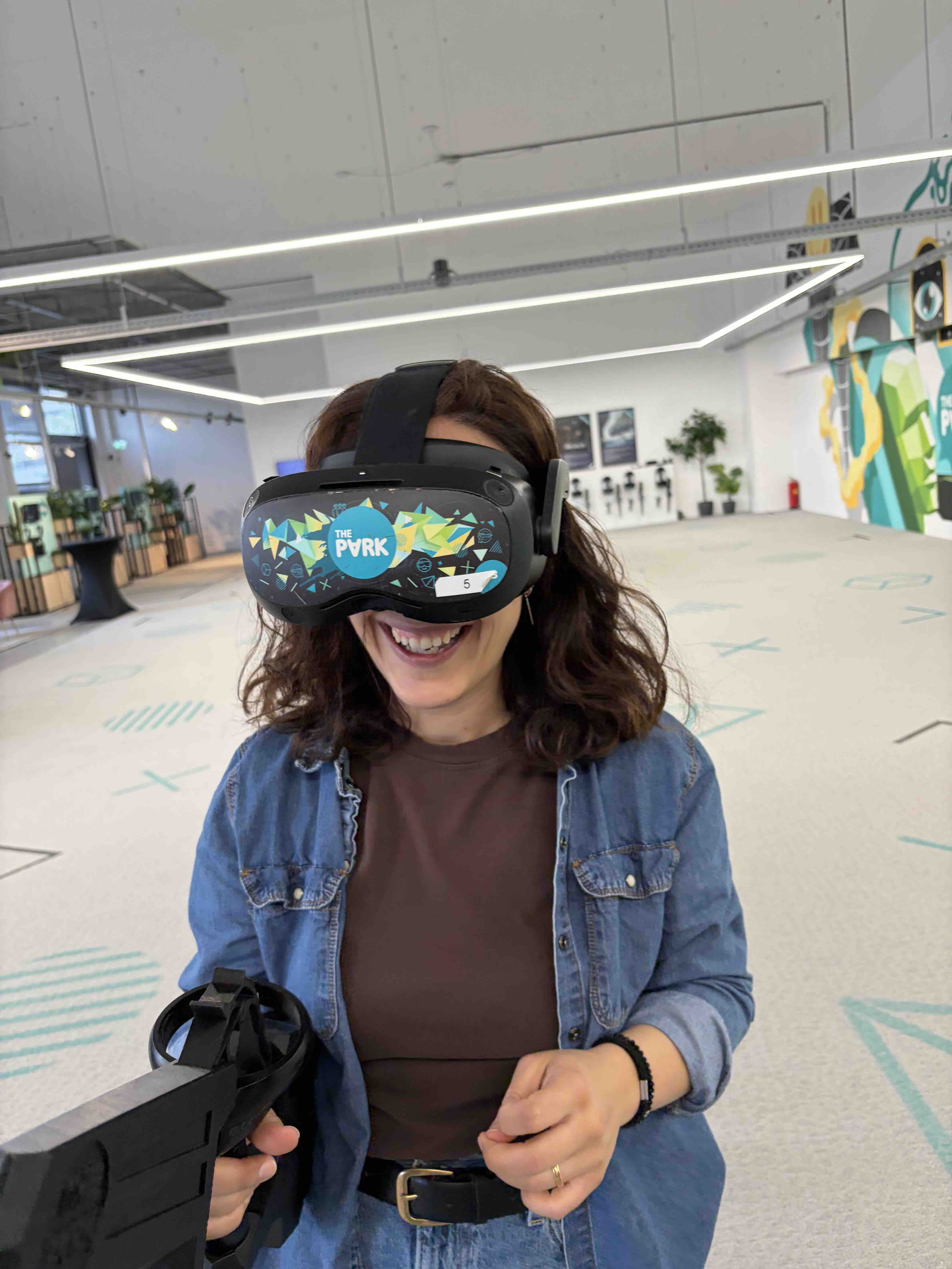 Vrouw die lacht met een virtual reality-headset op en een VR-controller in een moderne, ruime kamer.
