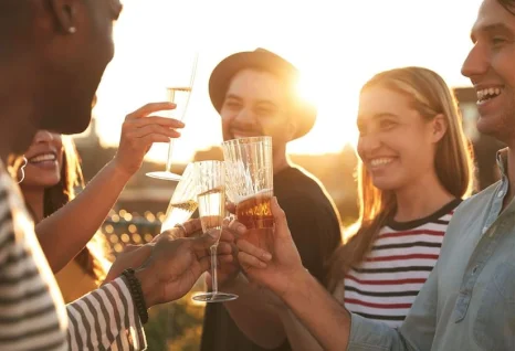 Fünf Personen auf einer Dachterrasse, die bei Sonnenuntergang mit Getränken anstoßen und lachen.
