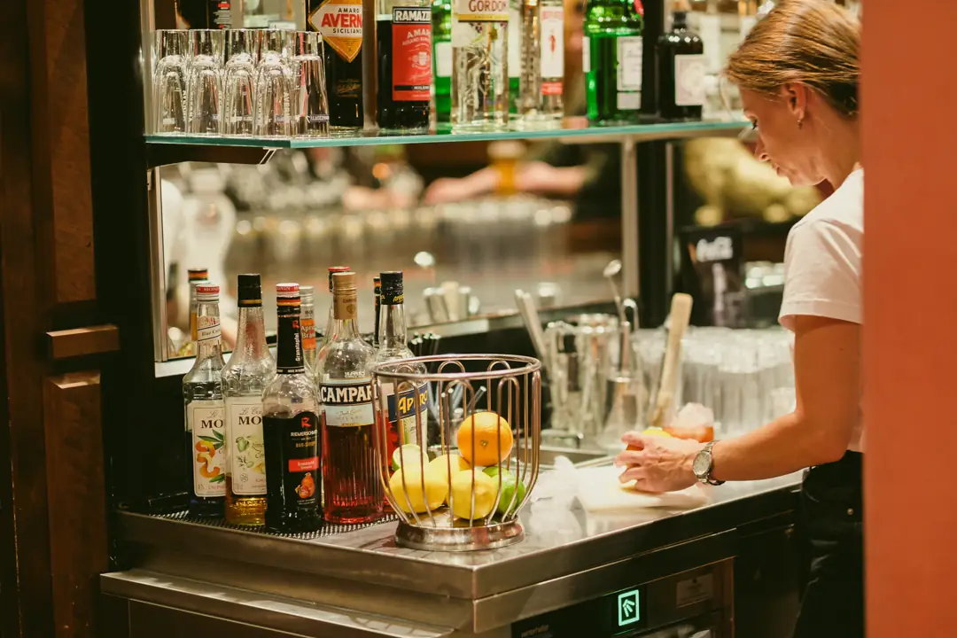 Bartender schneidet Früchte an einer Bar mit Spirituosenflaschen und Gläsern im Hintergrund.