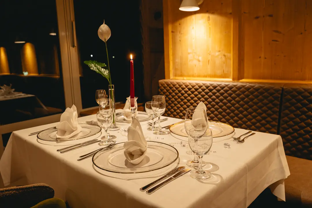 Eleganter Essbereich mit einem gedeckten Tisch für vier Personen, einer brennenden roten Kerze und einer weißen Blume in einer Vase.