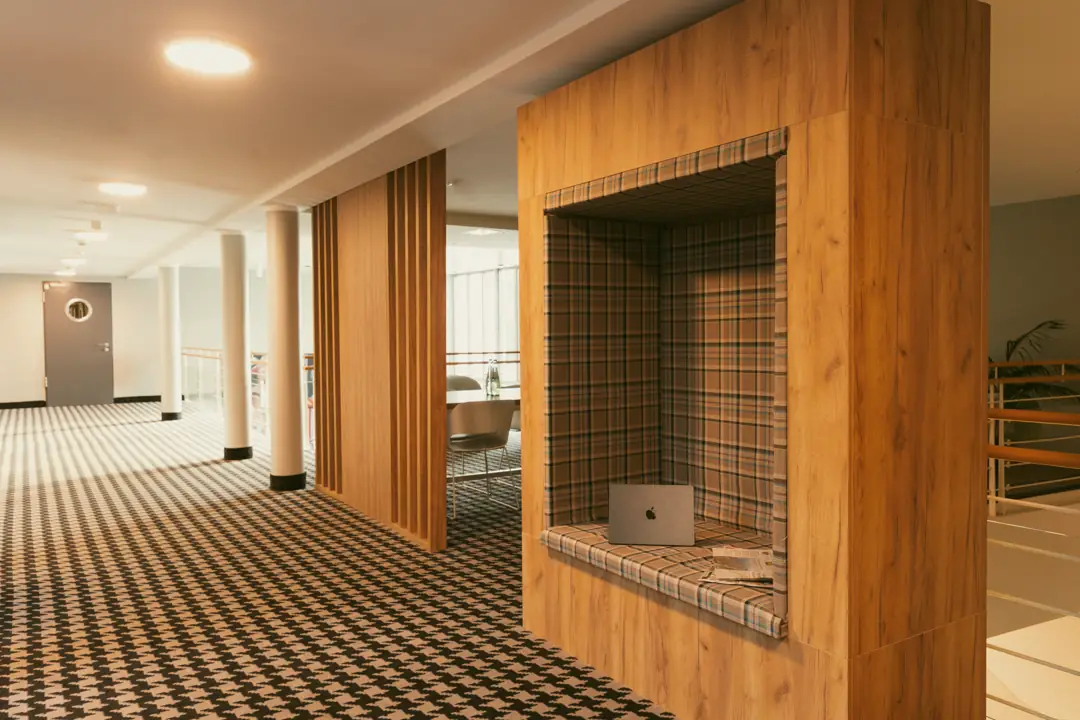 Moderner Flur mit karierten Teppichboden, Holzpaneelen und einer Nische mit kariertem Sitzkissen und offenem Laptop.