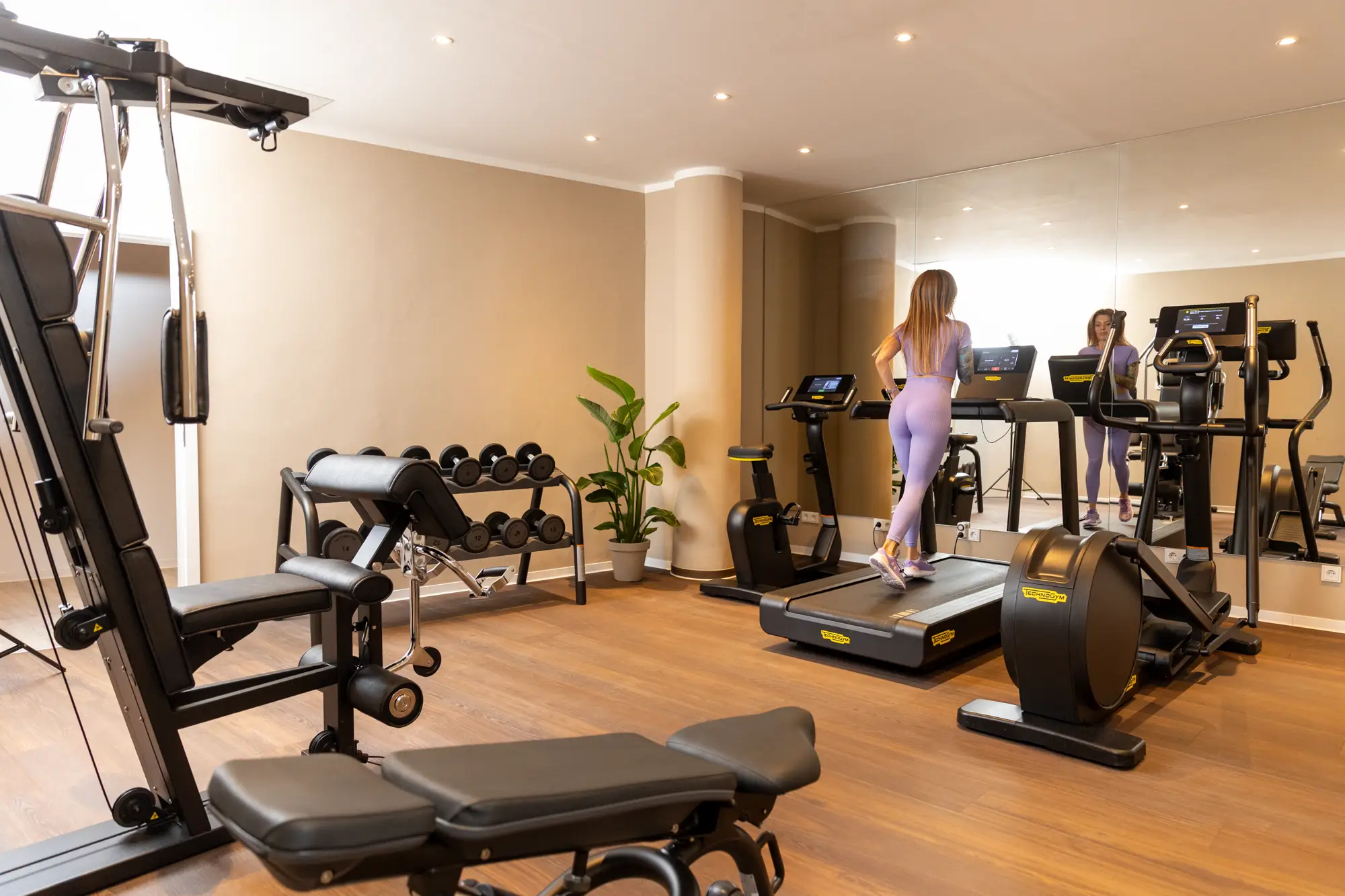 Frau in lila Sportkleidung läuft auf einem Laufband in einem modernen Fitnessraum mit Hanteln und Trainingsgeräten.