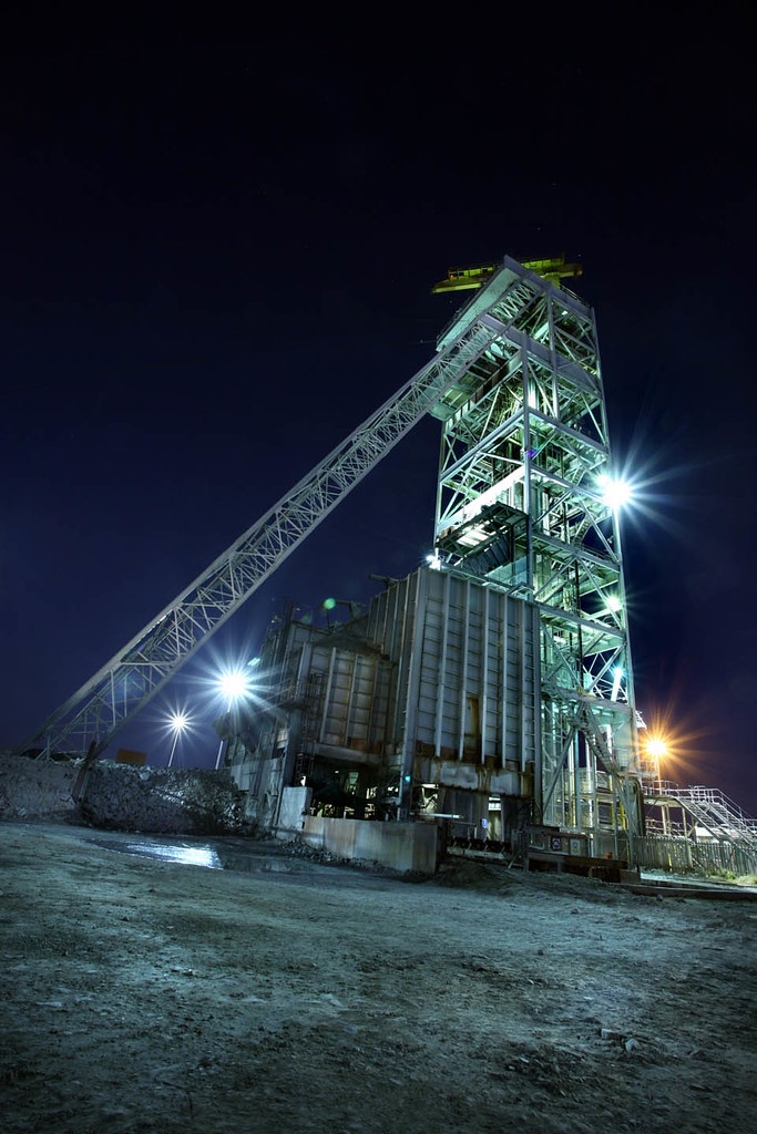 Illuminated mining headframe structure at night under a dark sky.