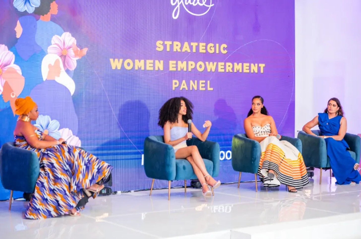 Four women seated on blue chairs on stage during a Strategic Women Empowerment Panel event.