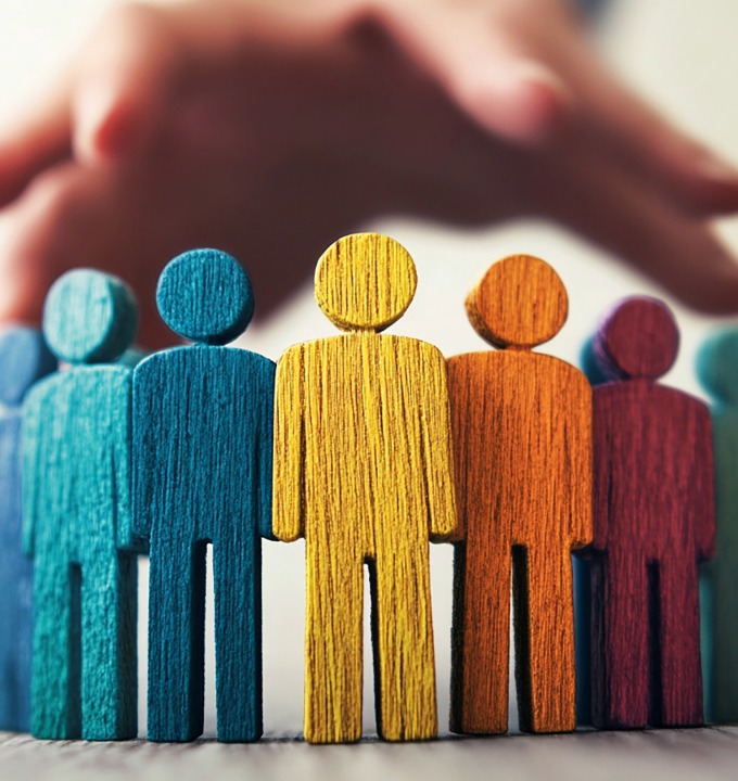 A hand protecting a diverse group of colorful wooden human figures standing in a row.