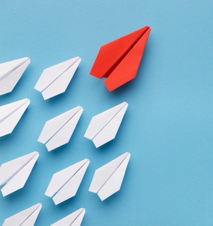 Red paper airplane leading a group of white paper airplanes on a blue background.