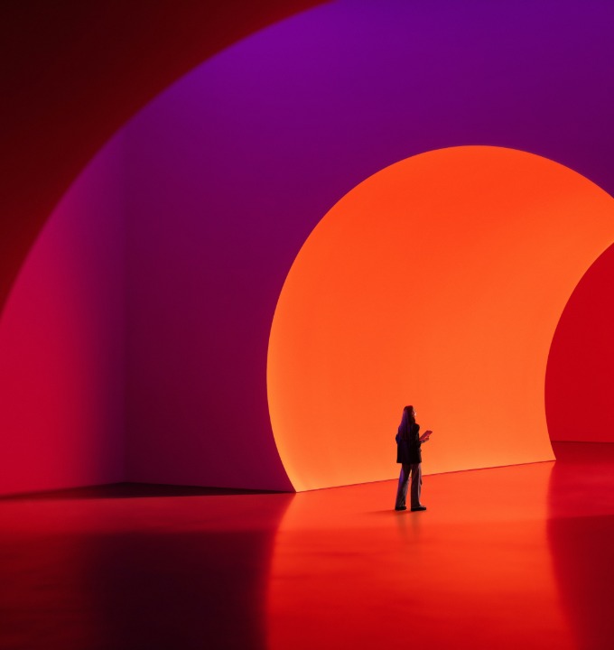 Person standing in a large room with glowing curved orange and purple walls.