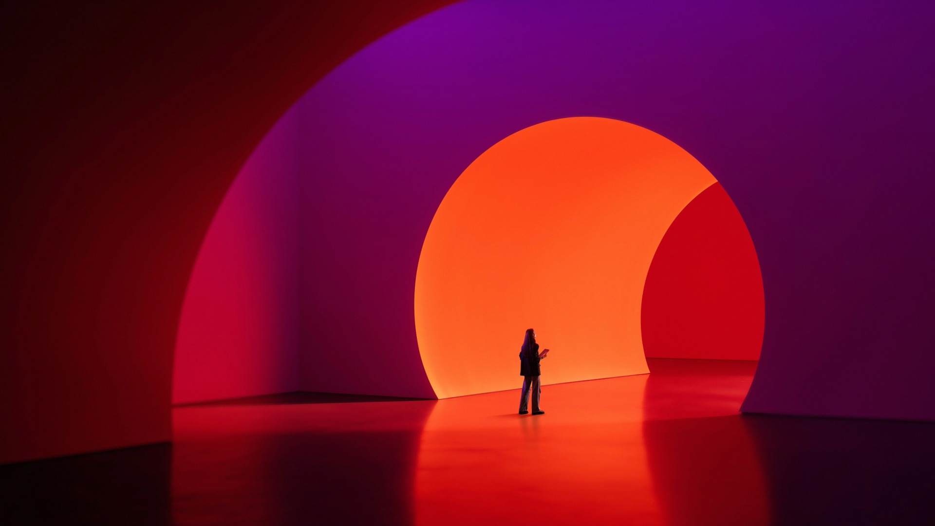 Person standing inside a large archway illuminated with vibrant red, orange, and purple lighting.
