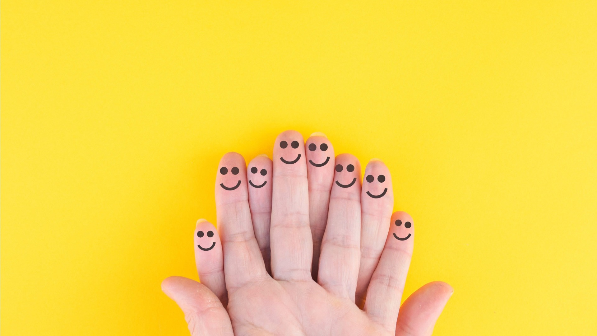 Fingers with smiley faces drawn on each fingertip against a bright yellow background.