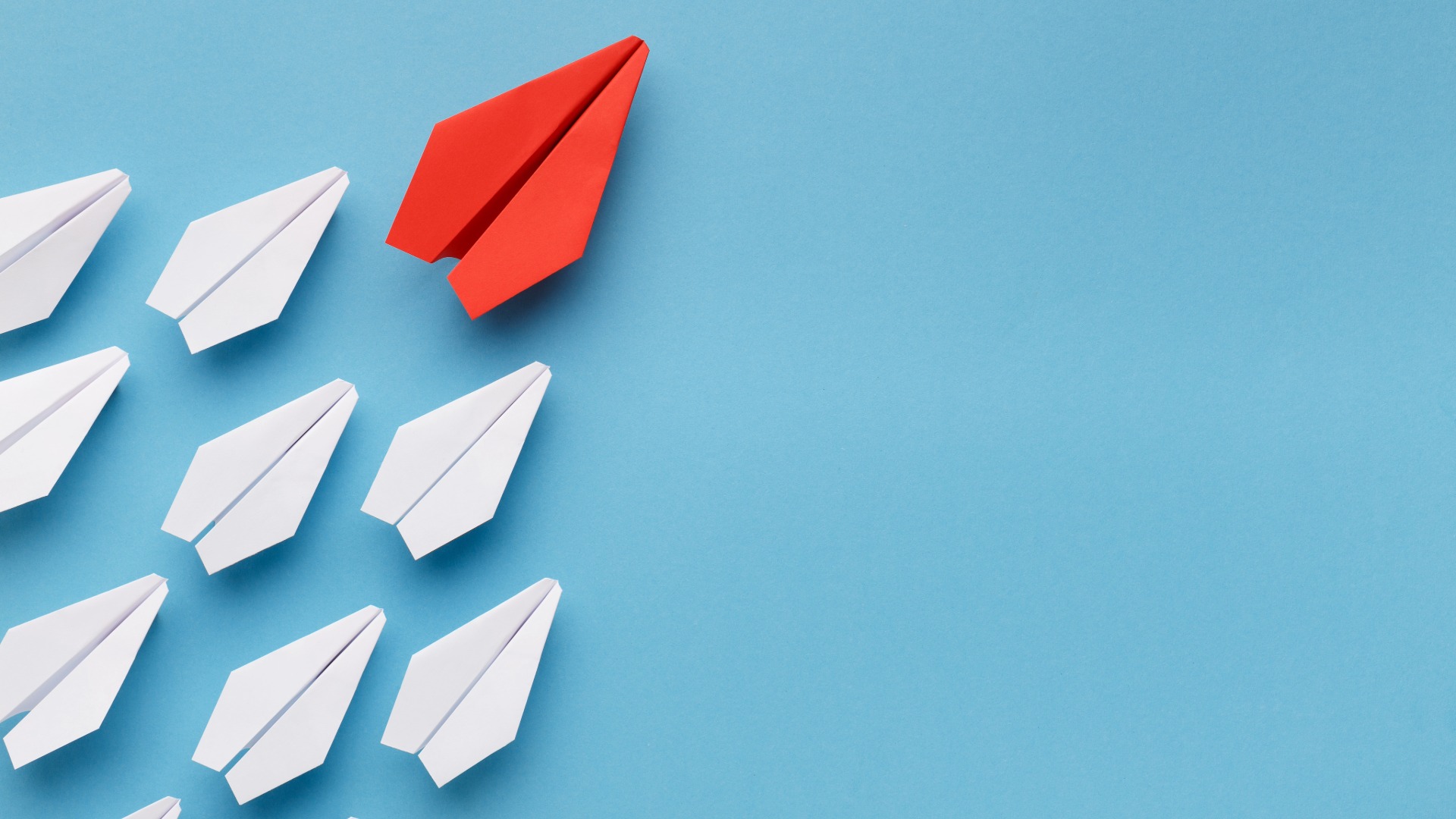 A red paper airplane flying ahead of several white paper airplanes on a blue background.