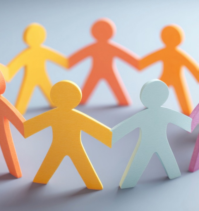 Close-up of colorful paper cutout figures holding hands in a circle on a gray surface.