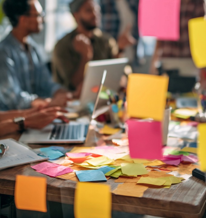 Team working at a table cluttered with colorful sticky notes and laptops in a collaborative meeting.