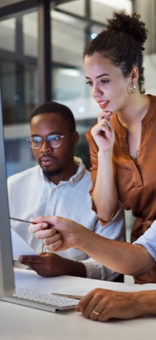Two colleagues looking at documents and a computer screen while discussing work in an office.