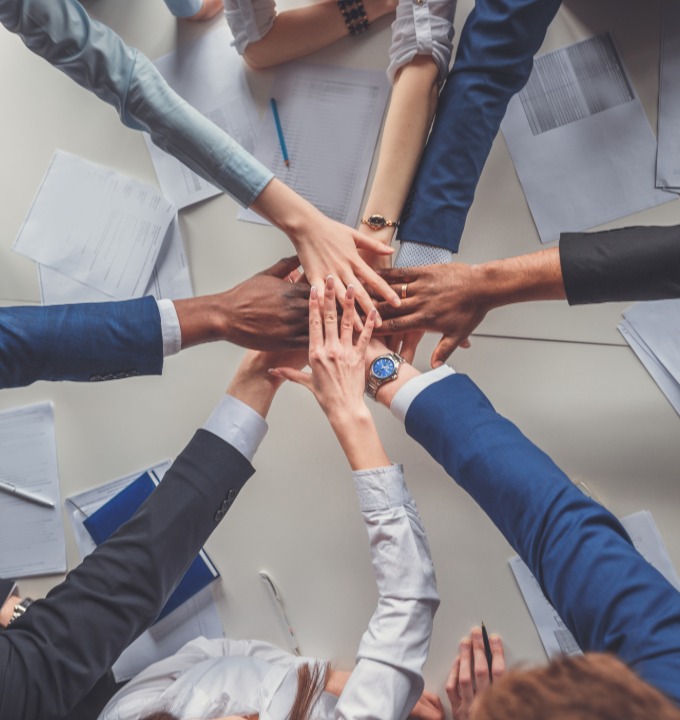 Diverse business team joining hands in center over desk with papers and pens.