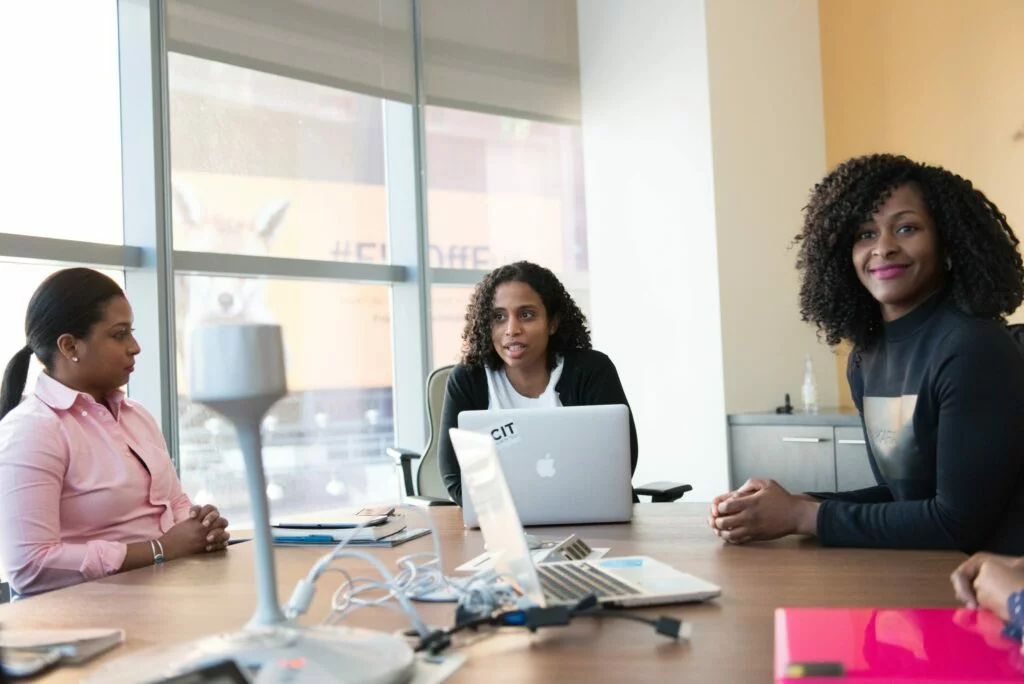 Three women seated around a conference table with laptops, engaged in a meeting in a modern office.