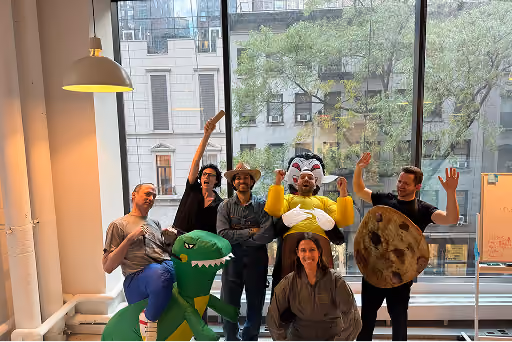 Group of six people posing indoors, including one in a dinosaur costume and one in a cookie costume.