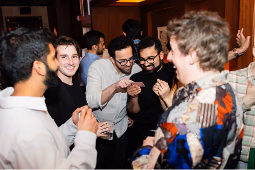 Group of friends laughing and looking at cards at a lively indoor party.