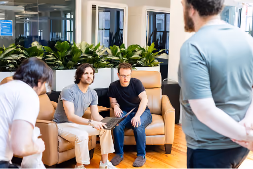 Four men in casual clothes having a discussion in a modern office with plants and leather chairs.