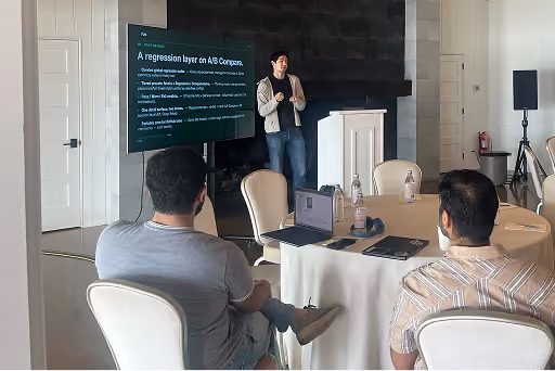 Man presenting regression layer slide to two seated men in a conference room with round table.