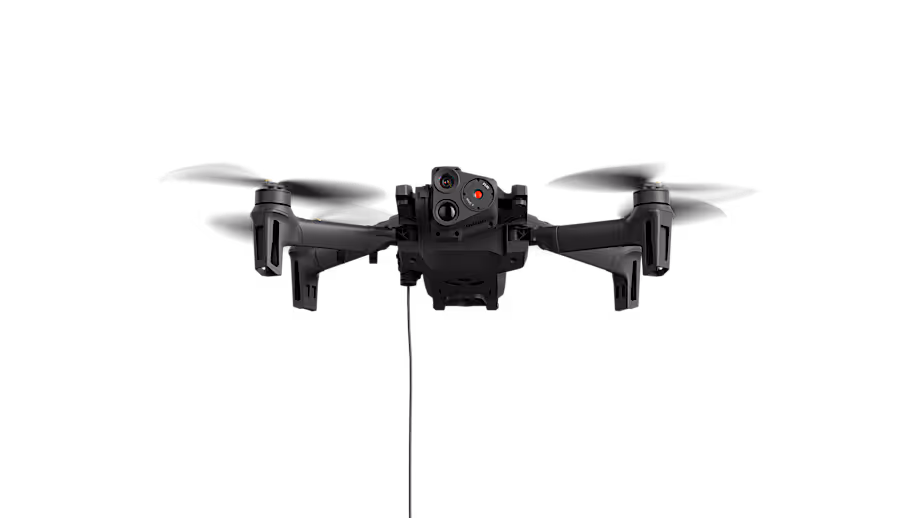 Black quadcopter drone with four propellers and dual front cameras suspended against a black background.