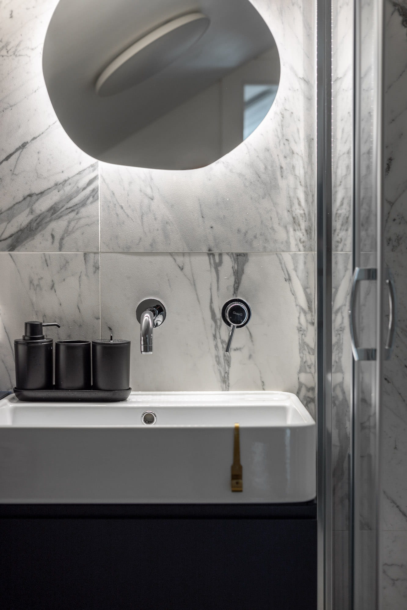 Moderna vannas istaba ar baltu izlietni, sienām ar marmora rakstu un apaļu apgaismotu spoguli.