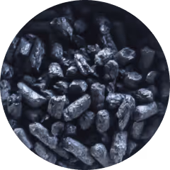 Cluster of shiny, irregularly shaped black pellets or granules, possibly charcoal or coal, on a dark background.