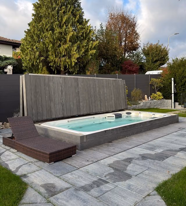 Eingebautes Swim Spa mit grauer Abdeckung auf Steinterrasse von oben