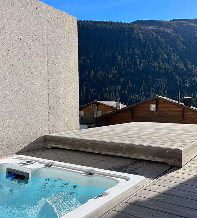 Whirlpool auf Holzterrasse in alpiner Berglandschaft mit Chalets