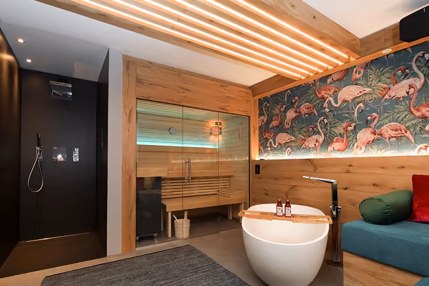 Moderner Wellnessbereich mit Sauna, Badewanne und tropischer Flamingo-Tapete.