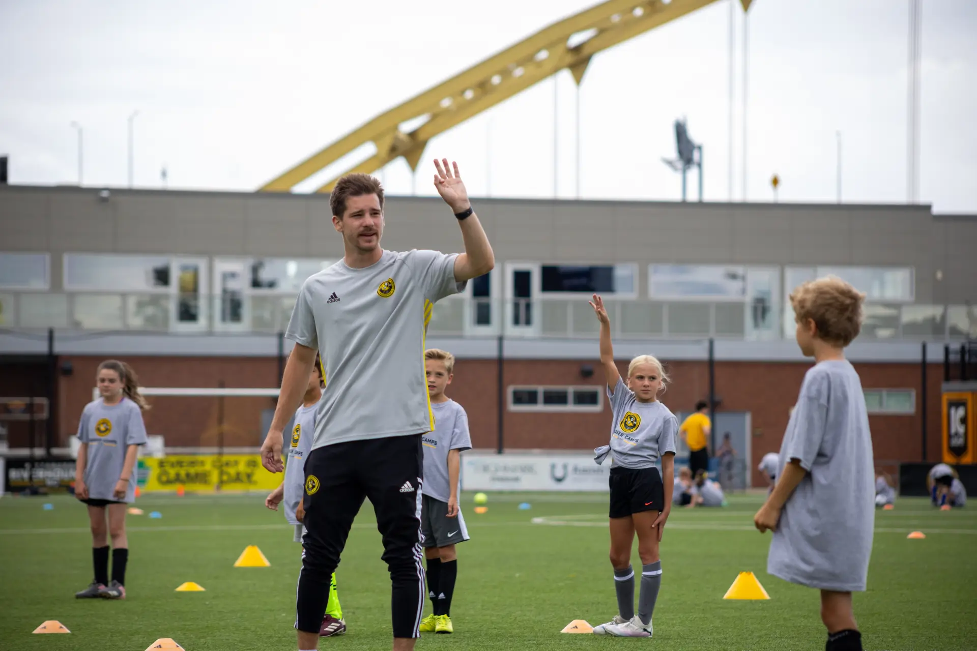 Academy coach leading a youth soccer clinic with Pittsburgh's bridges in the background