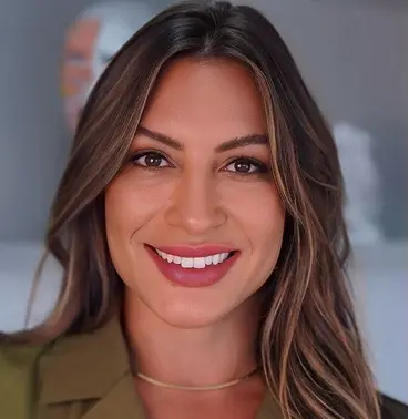 Smiling woman with long brown hair wearing a brown blouse and a gold necklace.