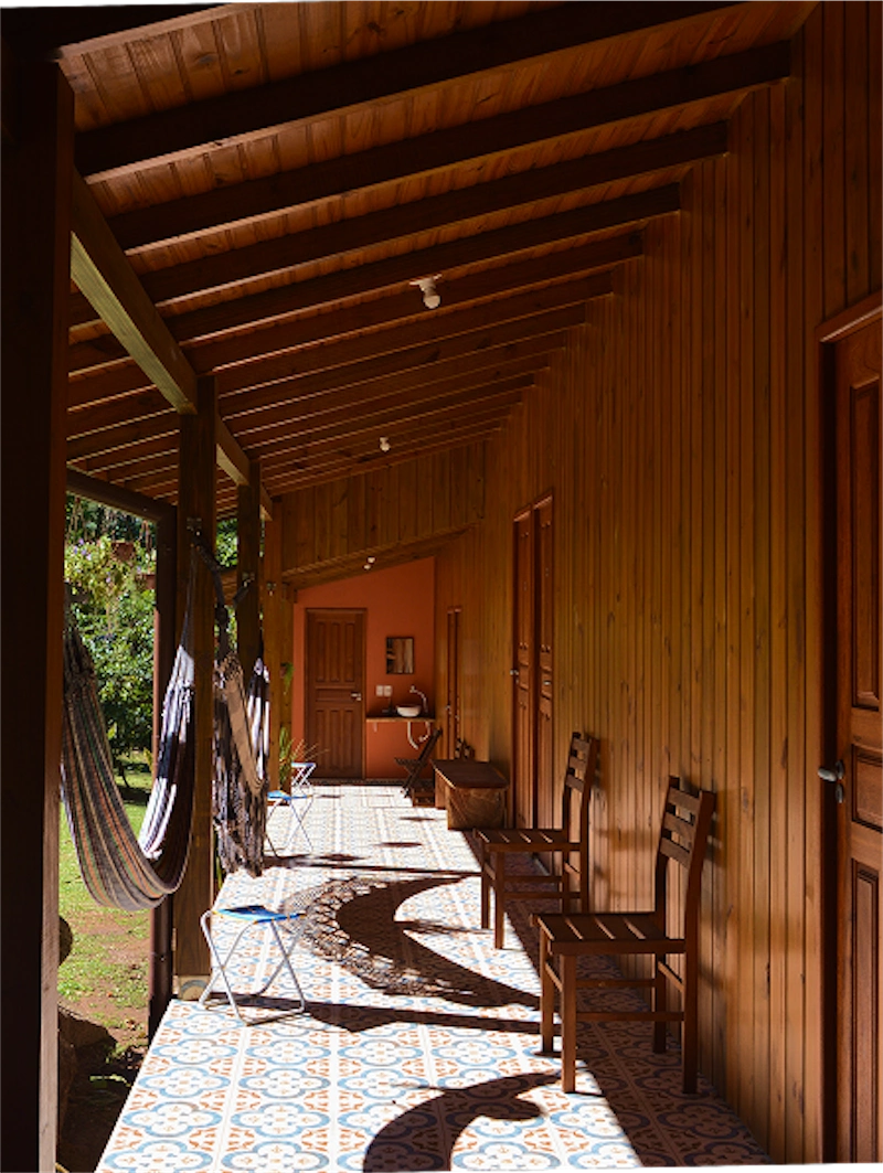 Wood-paneled porch with patterned tile floor, wooden chairs, hammocks, and sunlight casting curved shadows.
