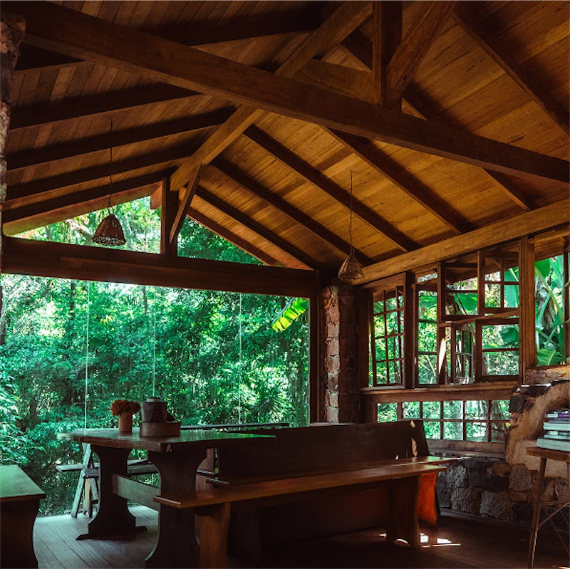 Cozy wooden cabin interior with large windows overlooking lush green forest.
