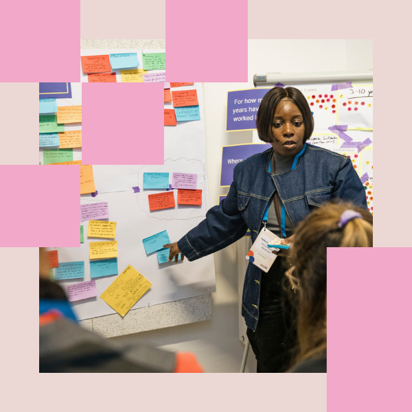 A person explaning something to a workshop group while pointing on a post-its wall.