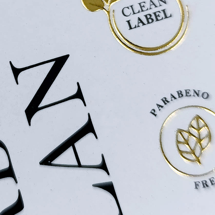 Detalhe de acabamento premium em Hot Stamping dourado sobre papel de alta gramatura.