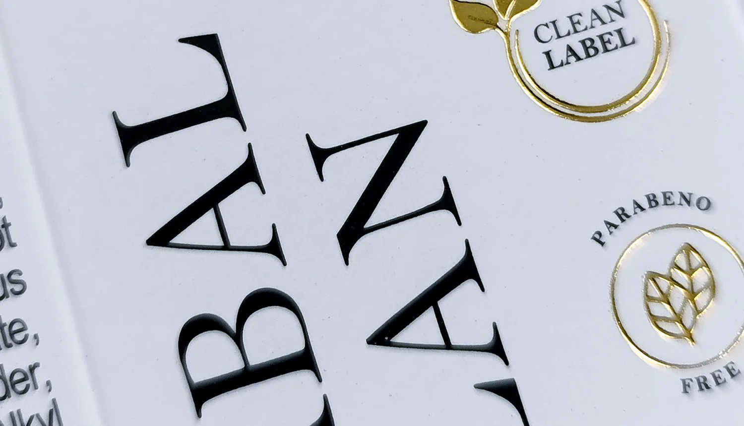 Detalhe em macro de acabamento premium com Hot Stamping dourado e relevo seco em rótulo Clean Label, demonstrando sofisticação e precisão técnica