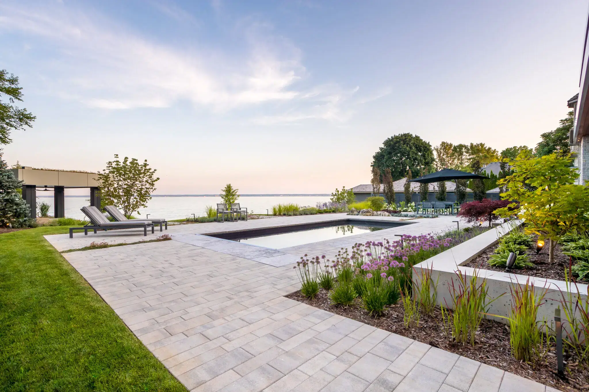 Paver patio design with lakeside pool and garden beds