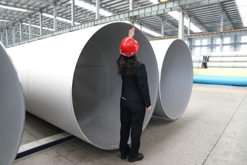 A worker inspecting metal pipes at a production site, the kind of installation a UK CBAM verifier will visit