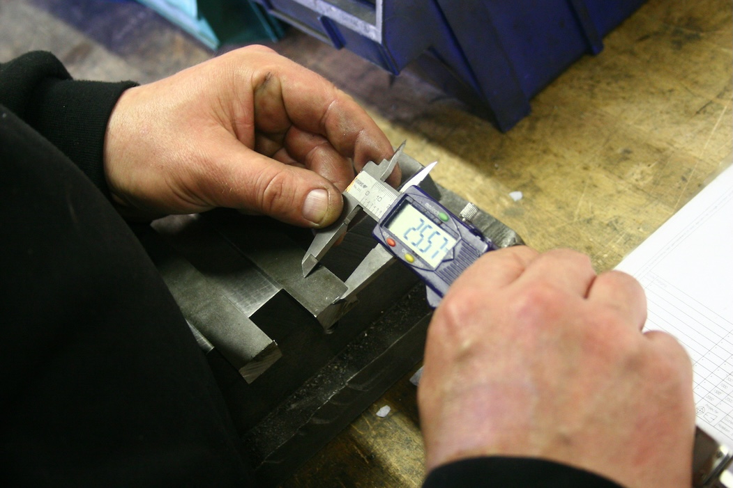 Measuring a metal part with digital callipers, reflecting the UK CBAM emissions and verification rules