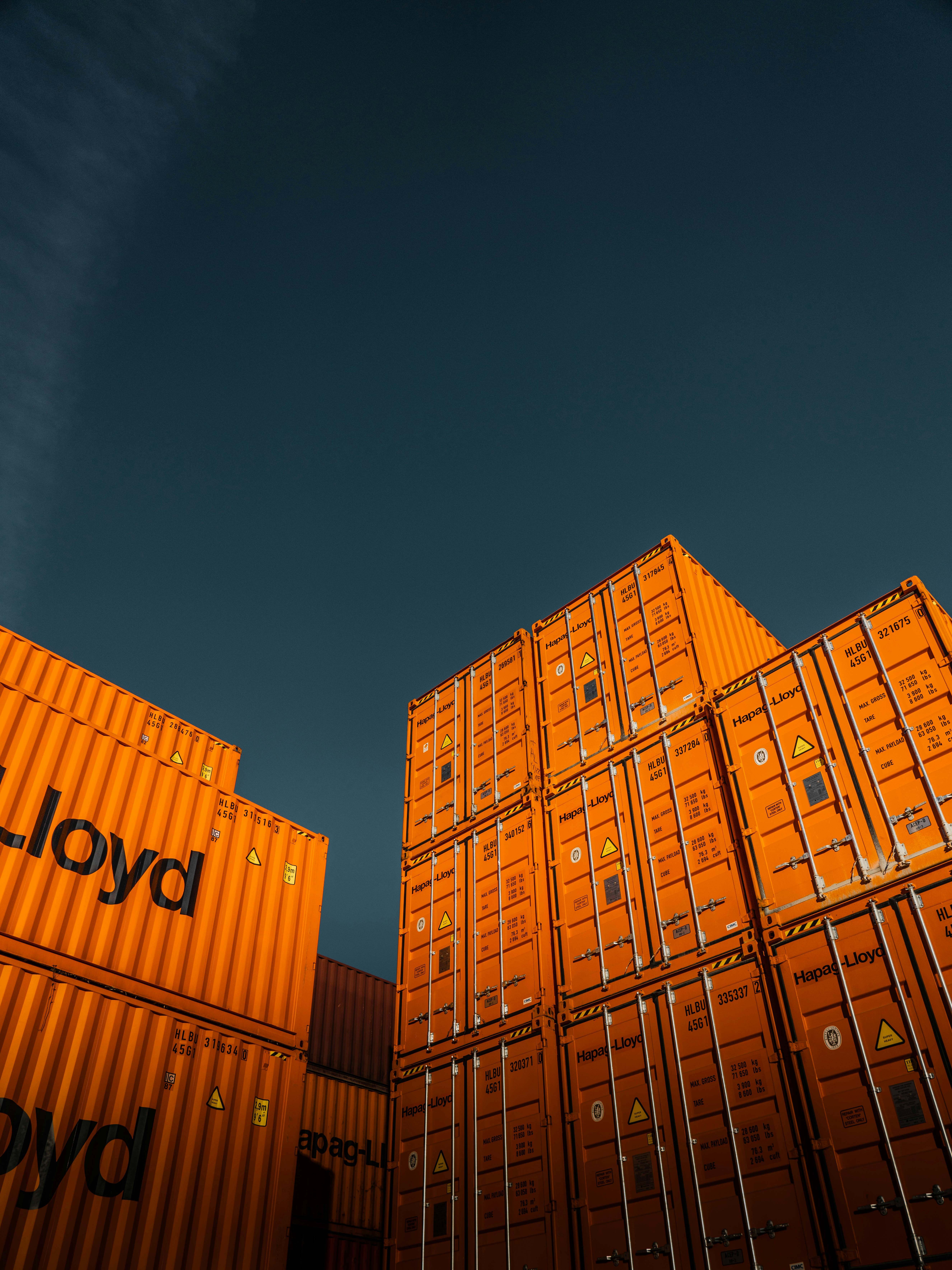 Stacked shipping containers, representing imports that will need CBAM certificates from February 2027