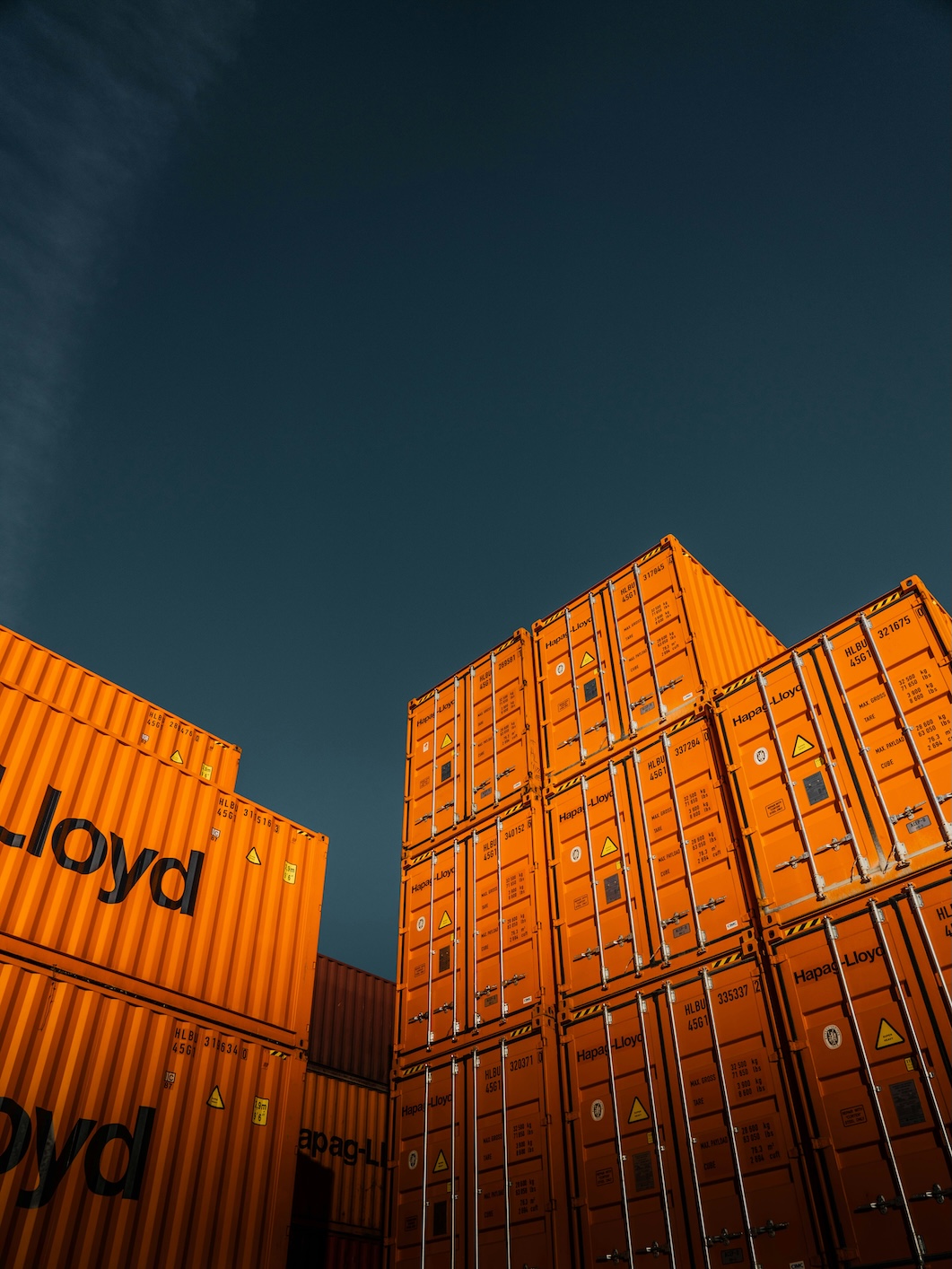 Stacked shipping containers, representing imports that will need CBAM certificates from February 2027