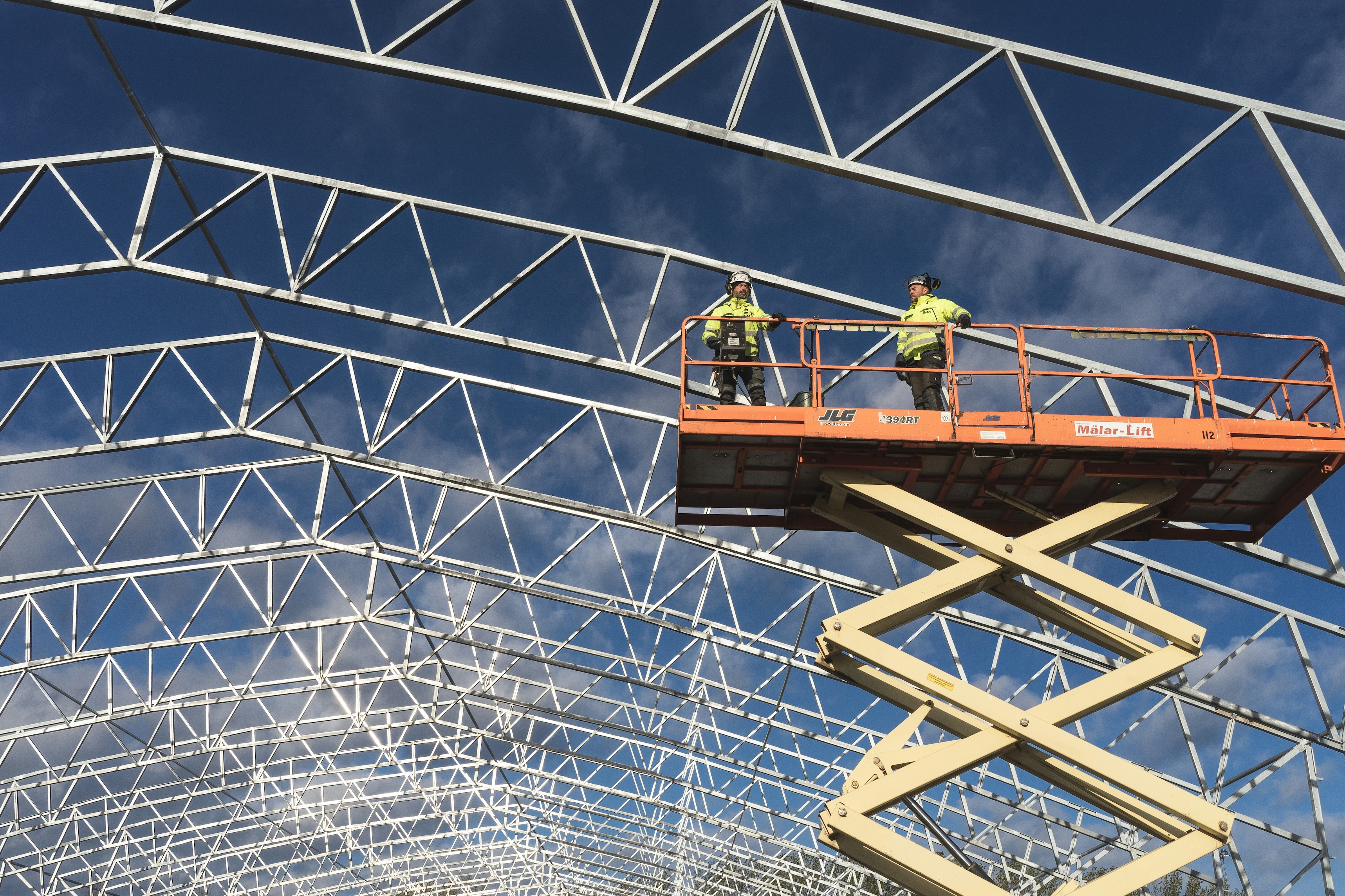 Workers on a lift beneath a steel roof frame, the kind of downstream product the CBAM extension targets