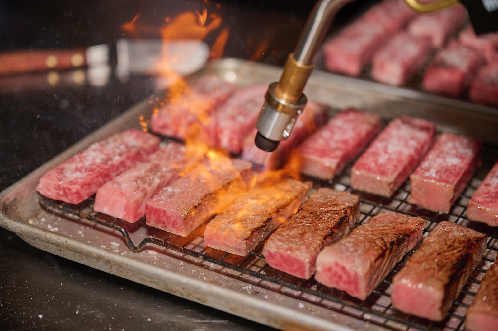 2 rows of tuna steaks being seared by a blow torch with flames