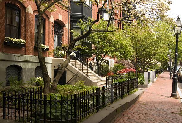 An image of homes with brick sidewalks and lamp posts trees and flowering plants in Beacon Hill known as one of the oldest neighborhoods in Boston.